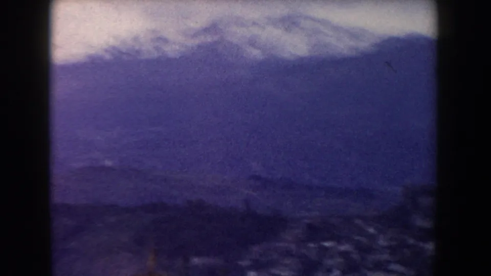 A soft 8mm view shows a distant mountain or shoreline beyond water, with purple-blue fading and visible film texture.