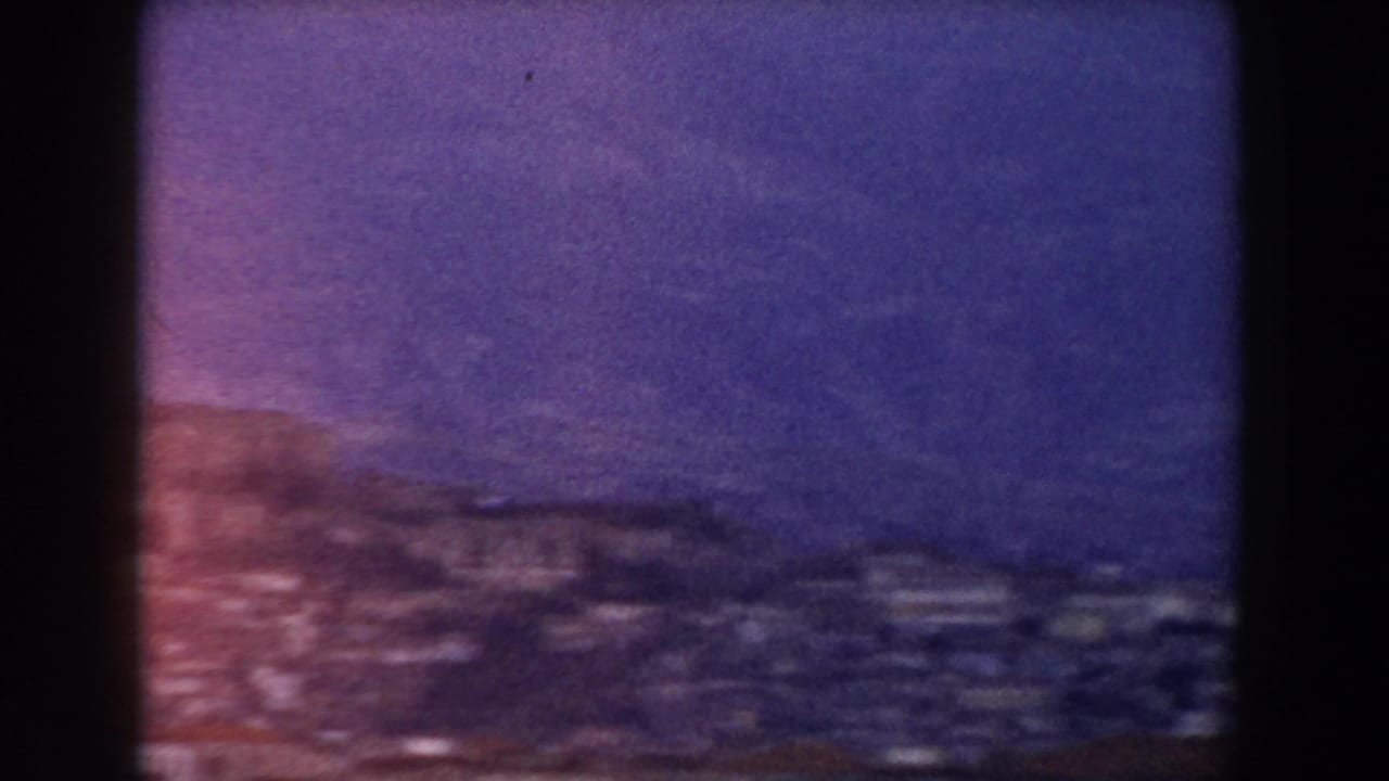 Dark hillside village under a purple-blue sky with soft 8mm grain.