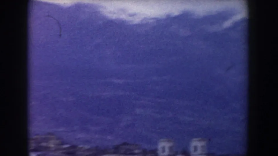 Soft 8mm frame from the Pisa-area clip with hazy mountains, dim village structures, and visible dark frame borders.