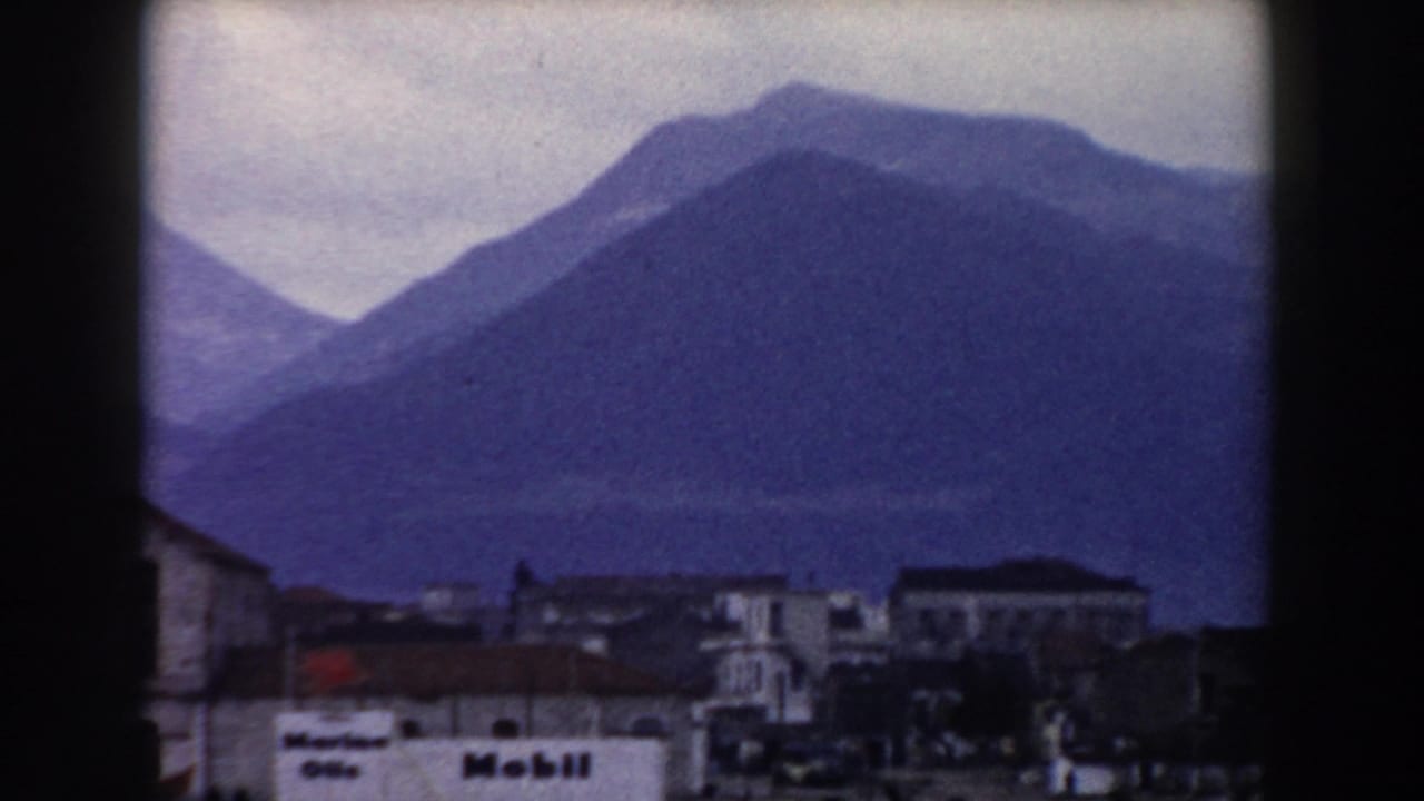 1959 8mm travel view in Pisa, Italy, showing layered mountains behind low town buildings and a white foreground facade.
