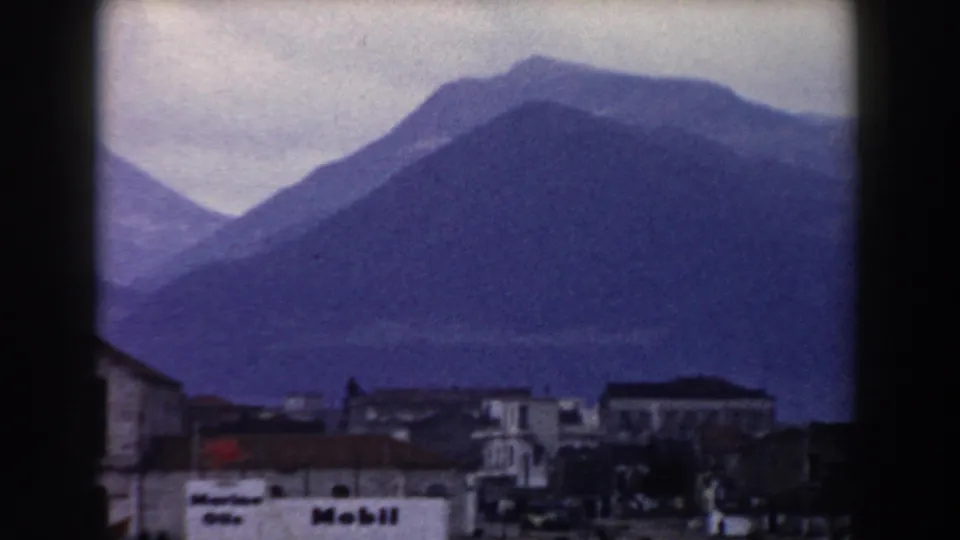 1959 8mm travel view in Pisa, Italy, showing layered mountains behind low town buildings and a white foreground facade.