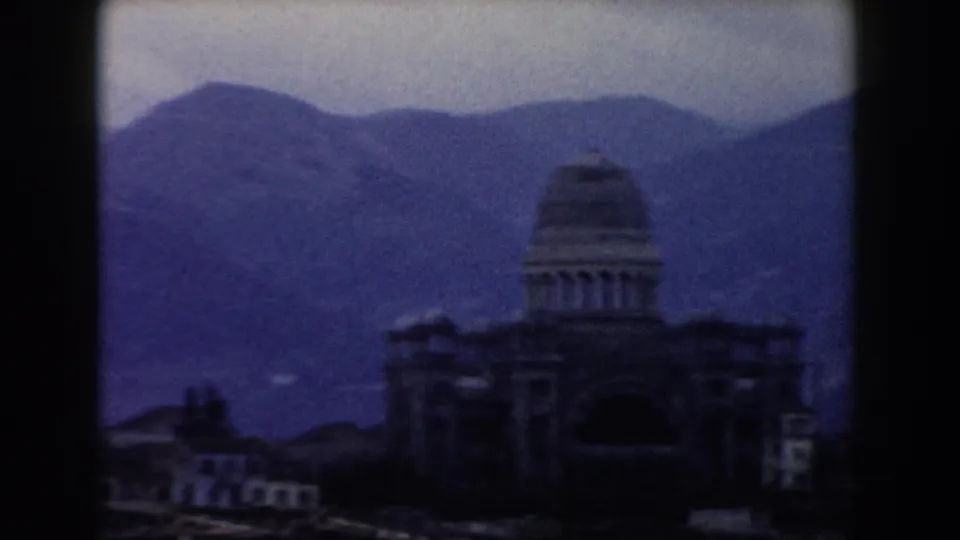 1959 8mm view in Pisa, Italy, with a domed structure and low buildings set against blue-purple mountain ridges.