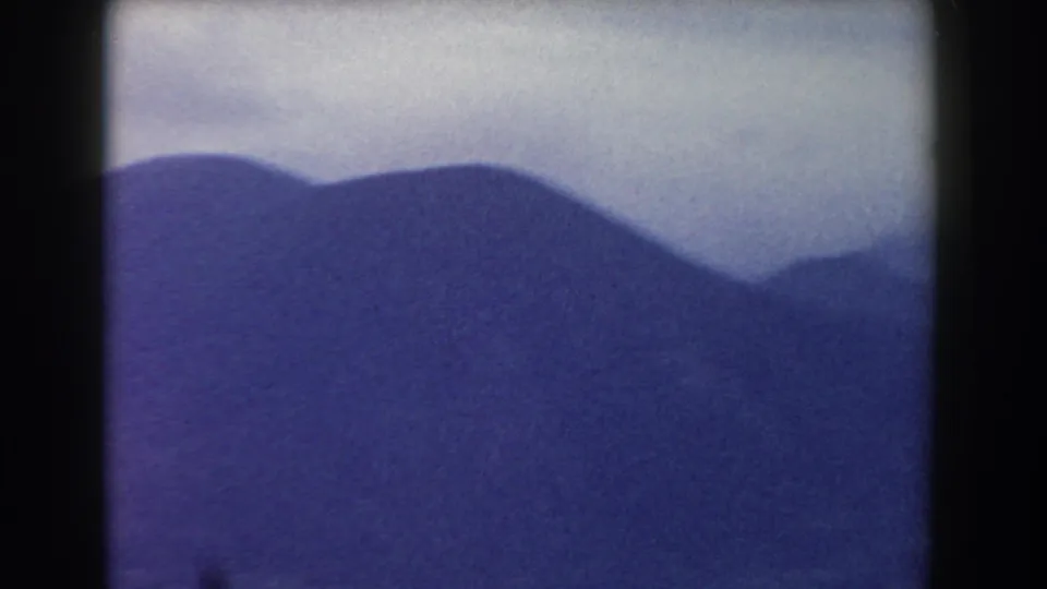 1959 8mm landscape frame from Pisa, Italy, showing hazy mountain silhouettes and a pale overcast sky.