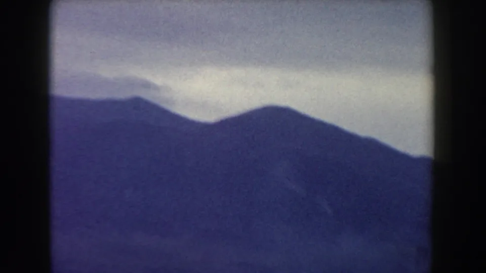 1959 8mm travel view in Pisa, Italy, with a dark ridge line and layered mountains fading into cloud.