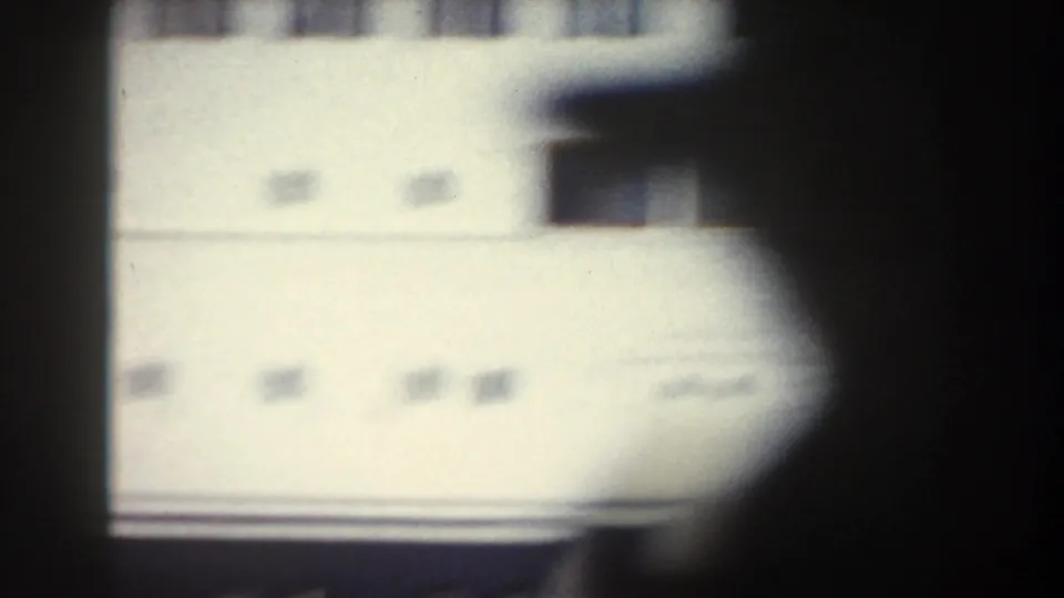 Obstructed 1959 home-movie view of a pale ship or building surface with small openings, heavily blurred by motion.