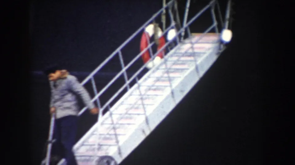 A man in a grey jacket leaves a ship on a metal gangway during the 1959 Pisa, Italy nighttime home-movie footage.