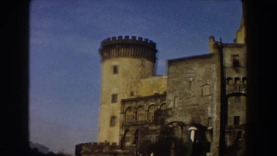 1959 Pisa travel footage frames the castle tower and adjoining stone facade with soft color and a dark vertical film border.