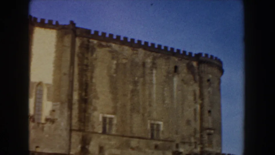 1959 Pisa home-movie frame showing the upper castle wall and rounded tower edge with crenellations against blue sky.