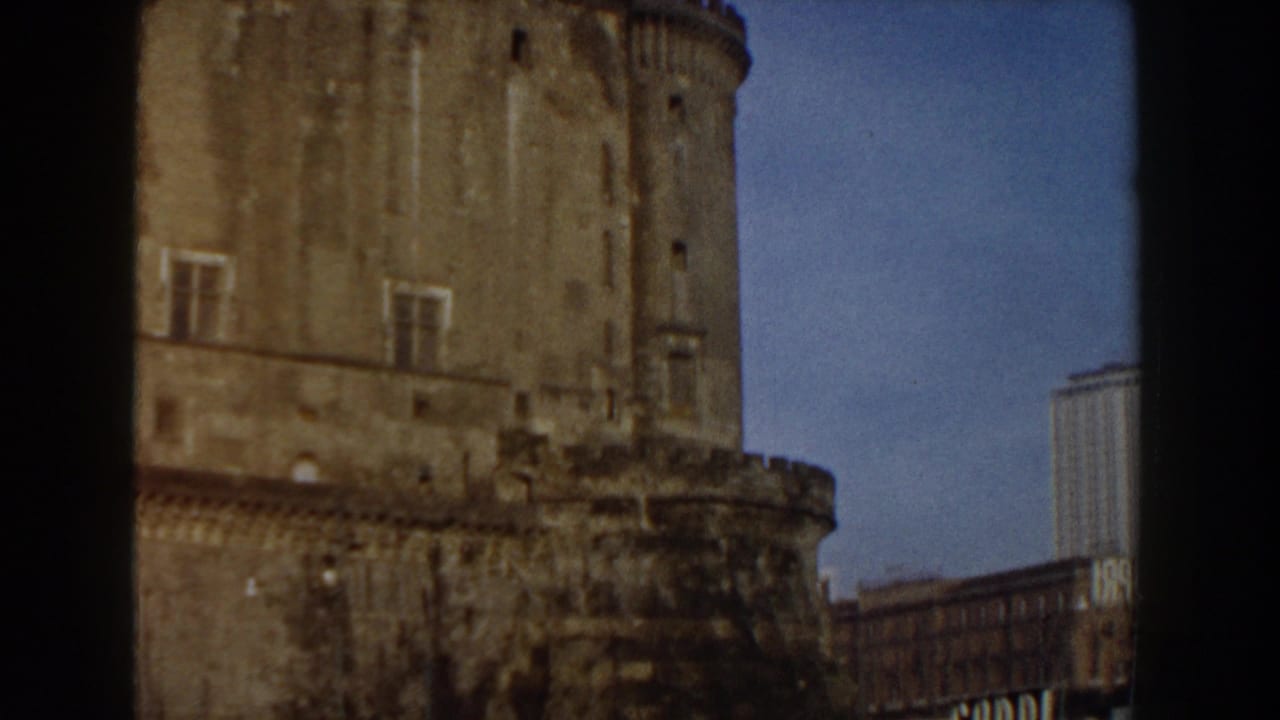 1959 8mm travel frame in Pisa, Italy, showing a large weathered stone tower and fortress wall with newer buildings behind it.