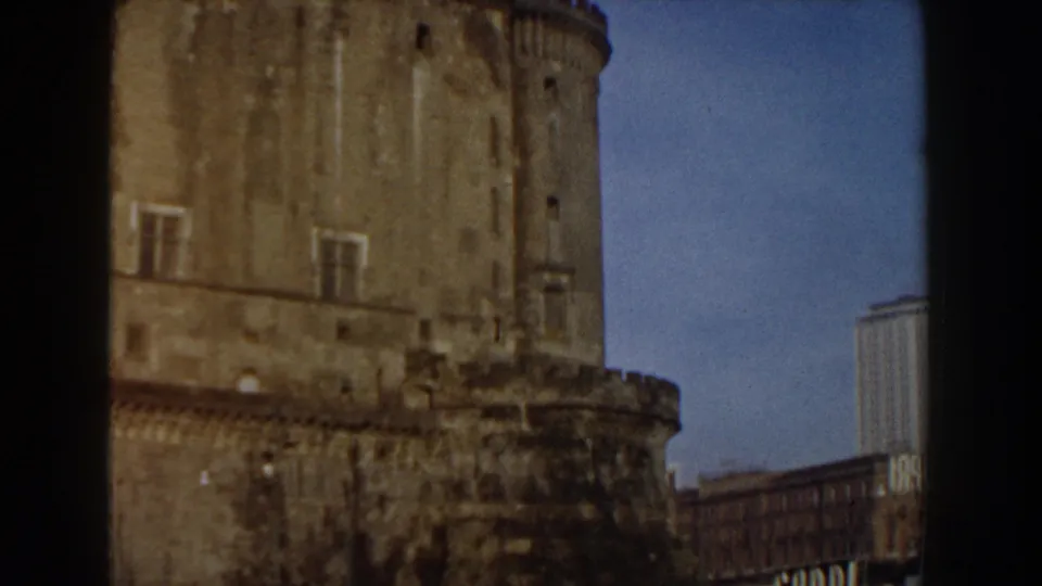 1959 8mm travel frame in Pisa, Italy, showing a large weathered stone tower and fortress wall with newer buildings behind it.