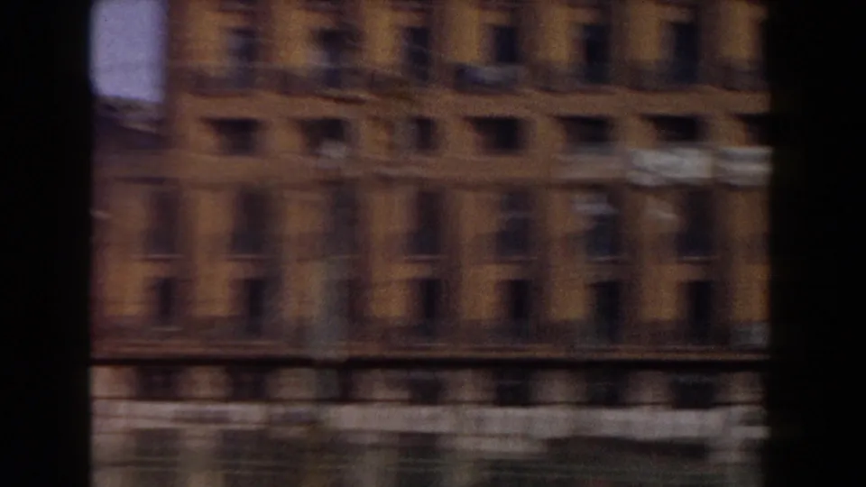 Motion-blurred 1959 8mm frame of a modern urban building facade, likely captured as the camera pans away from the fortress view.