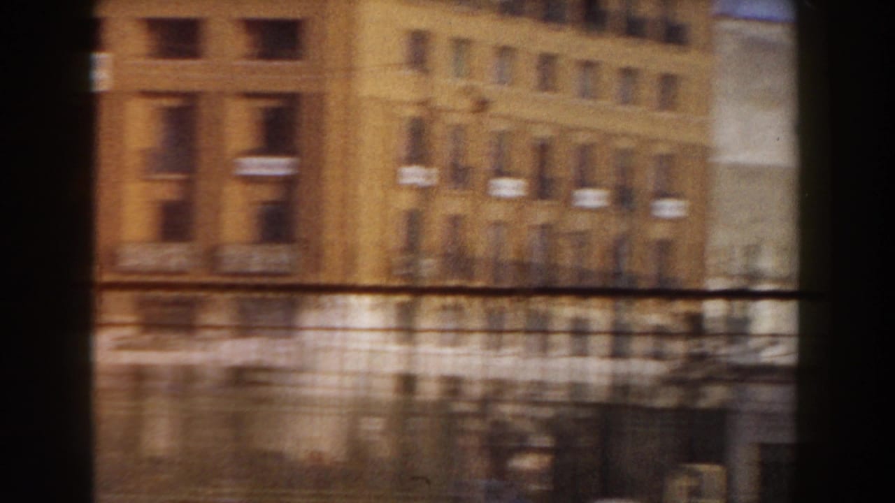 Blurred city buildings seen through a dark window or frame edge.