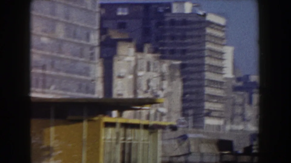 A 1959 Pisa city view shows a high-rise, older buildings, and a yellow railing or barrier from a moving vehicle.