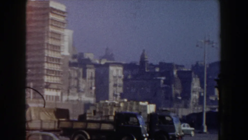 A moving 1959 Pisa view shows a tall brick building, distant cars, streetlights, and low urban rooftops.