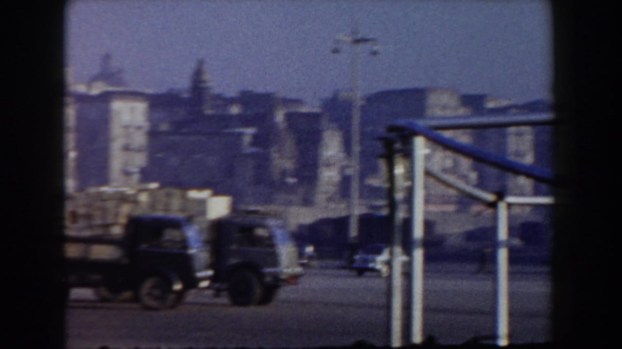 Port area with trucks, buildings, railings, and a blurred waterfront view.