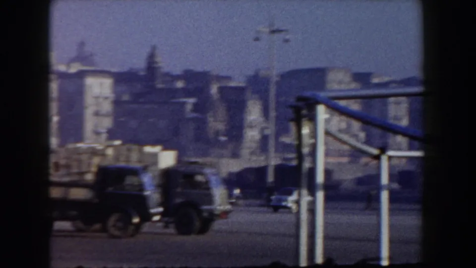 1959 Pisa-area port view with trucks, industrial buildings, railings, and soft 8mm focus from a shore position.