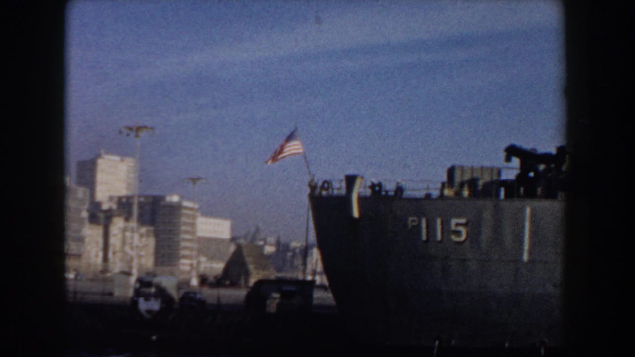 Docked naval ship marked P115 with an American flag beside a city waterfront.