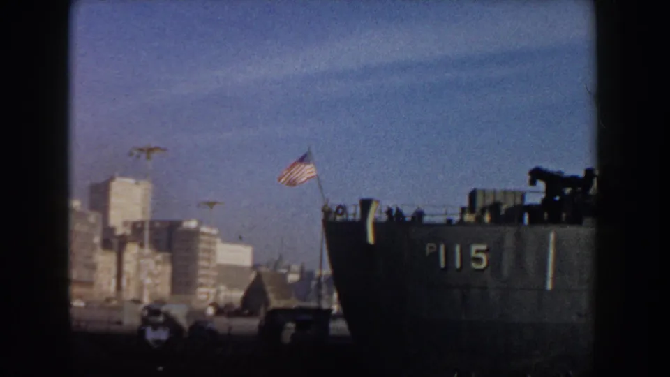 The docked P115-marked vessel remains near the Pisa waterfront, with an American flag above the stern area and mid-century buildings behind it.