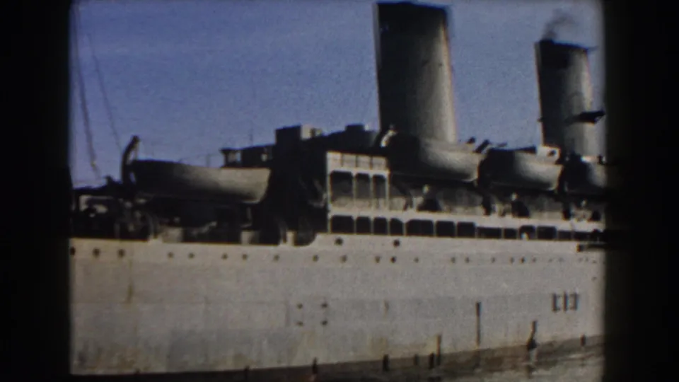 1959 Italy 8mm frame showing a docked ship's side with rows of portholes, deck equipment, and two visible funnels.