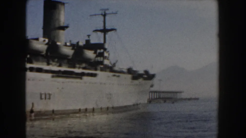 1959 Pisa, Italy home-movie still showing the ship closer to the bow, with a pier structure and hazy mountains across the water.