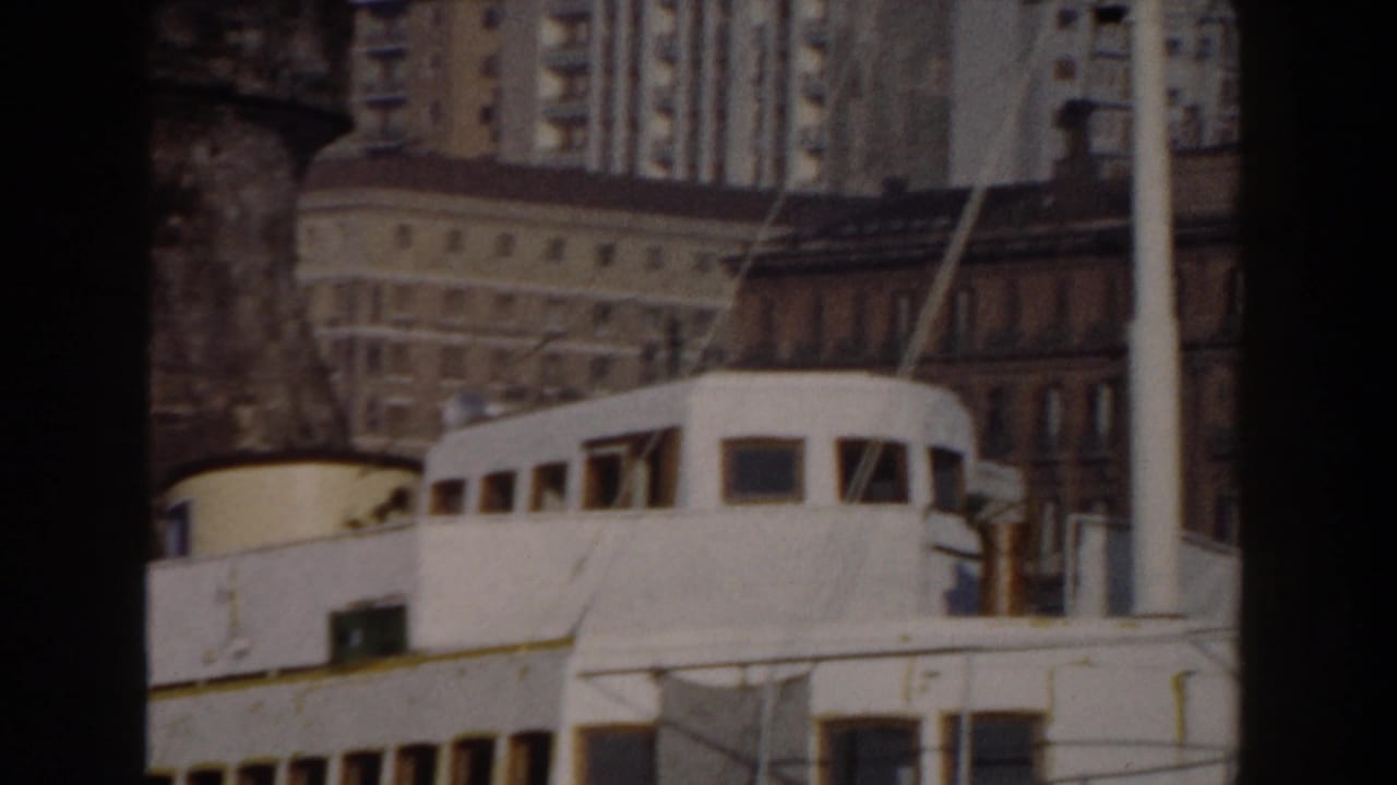 White boat cabin passing in front of waterfront buildings and taller city blocks.