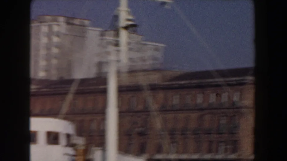 Moving 1959 Pisa waterfront view with a white mast or post, partial boat cabin, older facade, and pale multi-story building behind it.