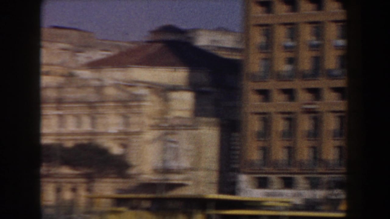 Weathered urban buildings seen through dark vertical foreground edges.