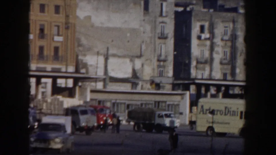 1959 Pisa street traffic with vintage cars, trucks, pedestrians, and a yellow van with visible lettering.