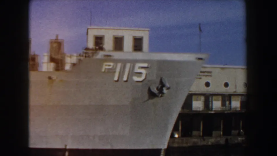 The P115-marked grey naval bow fills the frame as it passes a white building in the supported Pisa, Italy setting.