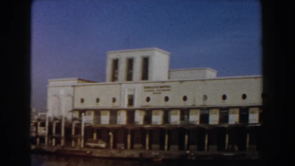 1959 Pisa waterfront view of a white modernist building with Banco di Napoli lettering, circular windows, dock structure, and water in front.
