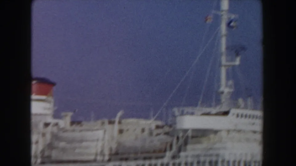 1959 Pisa, Italy home-movie frame showing part of a docked passenger ship with funnel, mast, rigging, and lifeboat shapes.