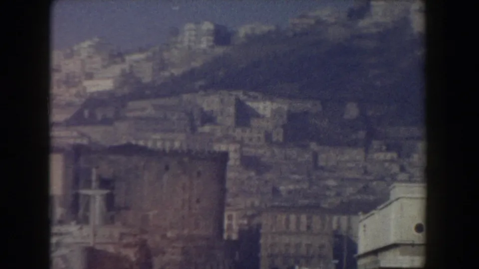 1959 8mm view of Pisa, Italy, showing a soft, hazy cityscape with pale historic facades and dense rooftops.