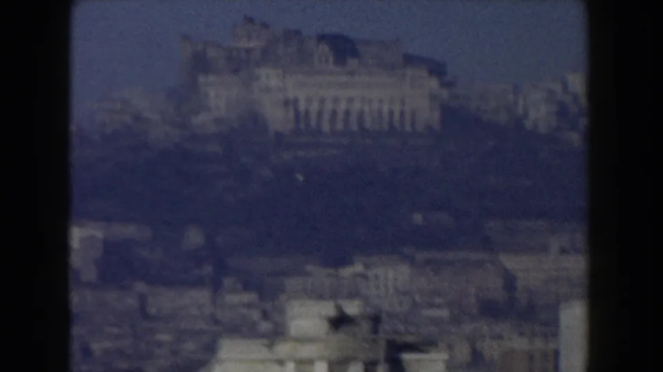 1959 8mm frame of Pisa, Italy, with a large distant historic building above a darker, hazy urban foreground.