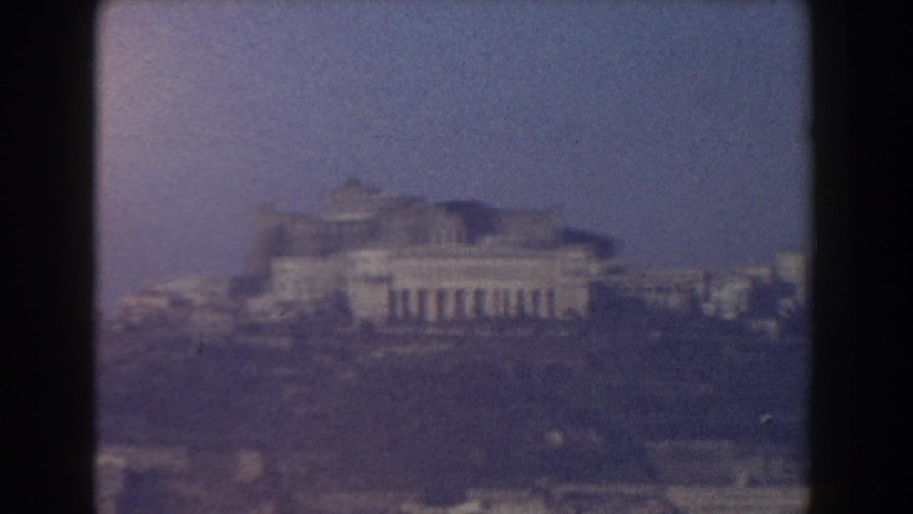 Distant pale buildings on a hazy skyline under blue sky, framed by dark 8mm borders.