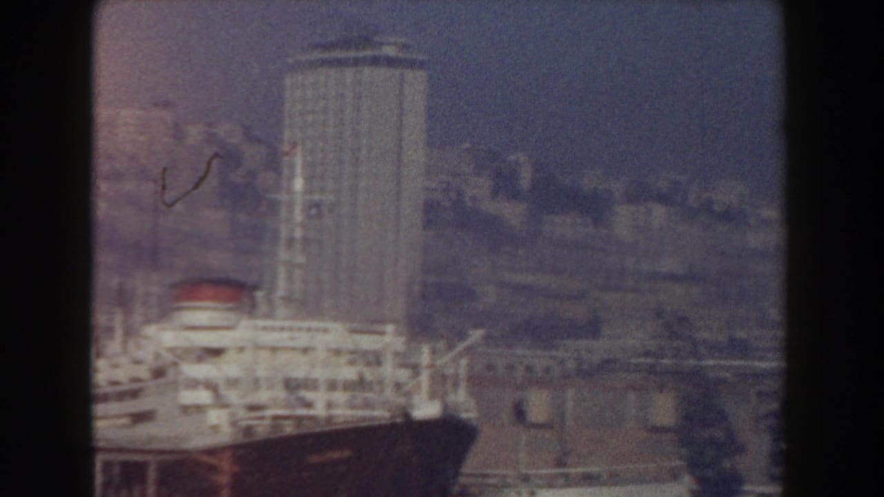 1959 Pisa, Italy home-movie frame showing a large ship beside tall waterfront buildings and industrial harbor structures.