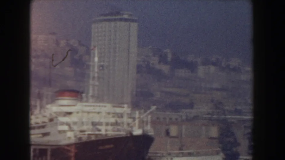 1959 Pisa, Italy home-movie frame showing a large ship beside tall waterfront buildings and industrial harbor structures.