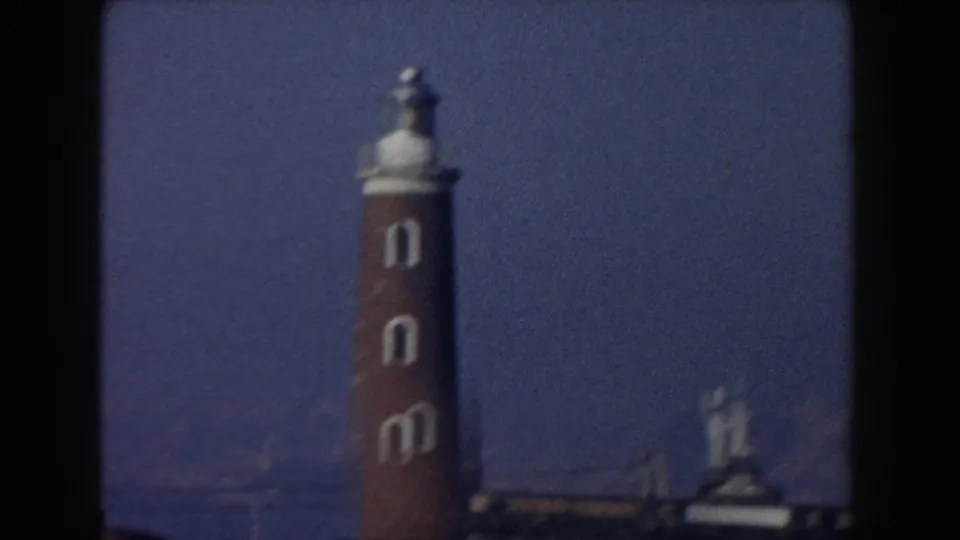 1959 Pisa, Italy frame centered on a red brick lighthouse with white arched openings and a small statue-like figure at the top.