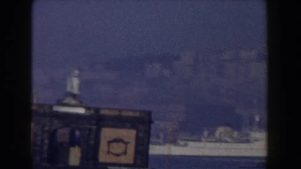 1959 Pisa, Italy home-movie view of a waterfront structure topped by a small statue, with a pale ship or boat behind it.