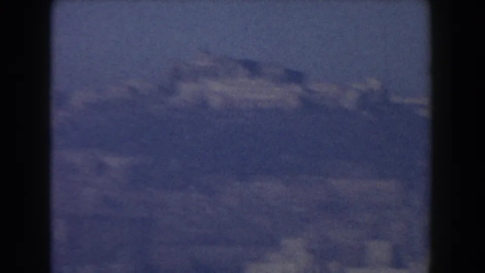 Soft, blue-tinted 1959 8mm view of Pisa with hazy hills and faint city buildings in the distance.