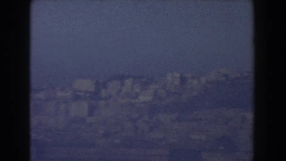 1959 8mm view near Pisa, Italy, showing a soft, hazy city and hillside landscape in the distance.