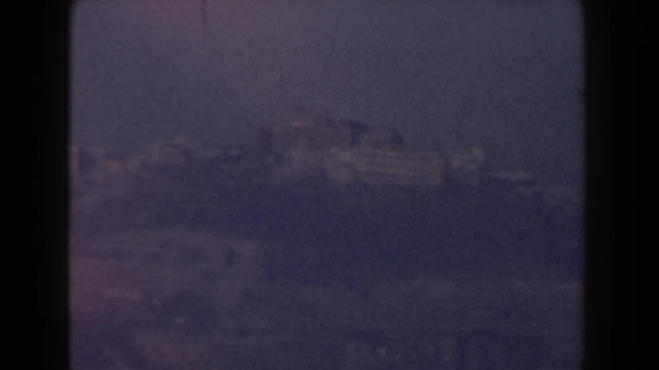 Soft 8mm frame of a distant ridge and urban structures near Pisa, Italy, with low contrast and purple-blue haze.
