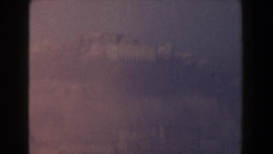 Hazy 1959 home-movie view near Pisa, Italy, with blurred valley terrain and low city structures in the distance.