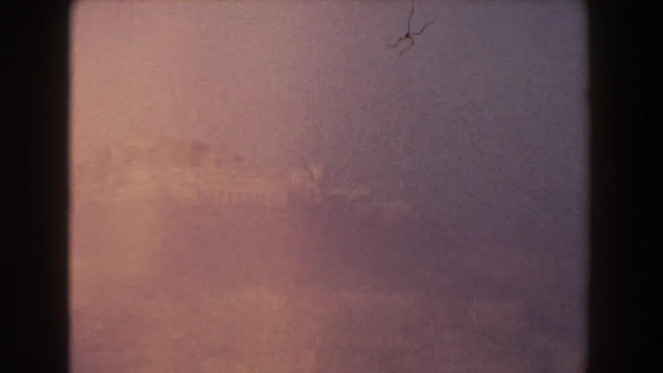 Pisa 1959 8mm frame showing a barely legible distant horizon or ruins through pink-orange exposure, grain, and small scratches.