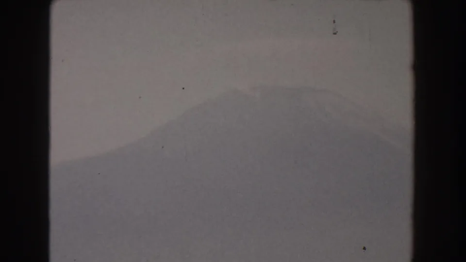1959 Pisa, Italy 8mm frame showing a low-contrast mountain ridge beneath a pale sky, with grain, dust, and dark film gate edges.