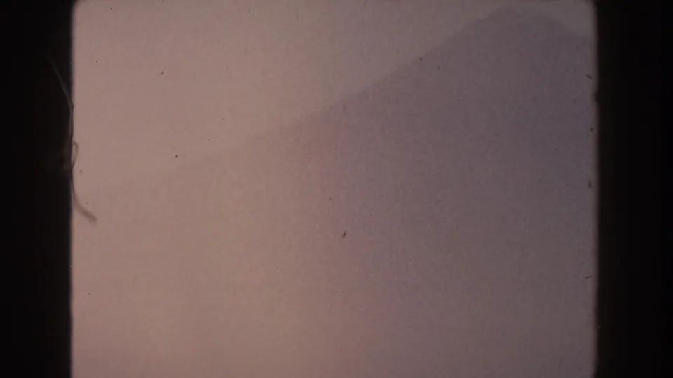 1959 Pisa, Italy 8mm frame showing a muted mountain slope under haze, with rounded frame edges and film dust.