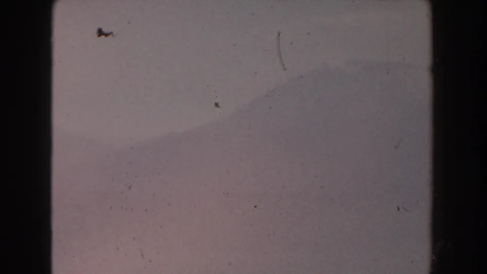 1959 Pisa, Italy 8mm still of a distant mountain ridge softened by haze, crossed by small scratches and dust marks.