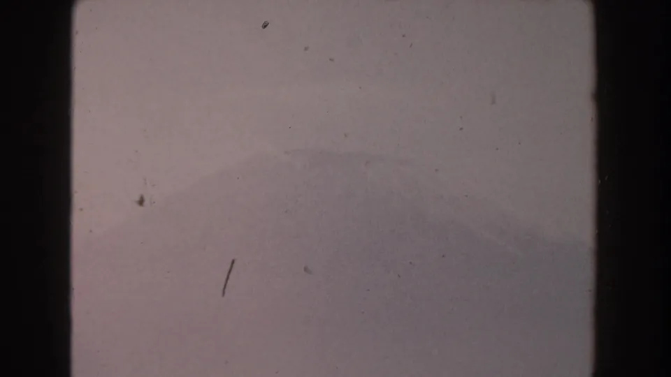 1959 8mm footage from Pisa showing a hazy, pale sky with a faint mountain or hillside silhouette beyond dark film gate edges.