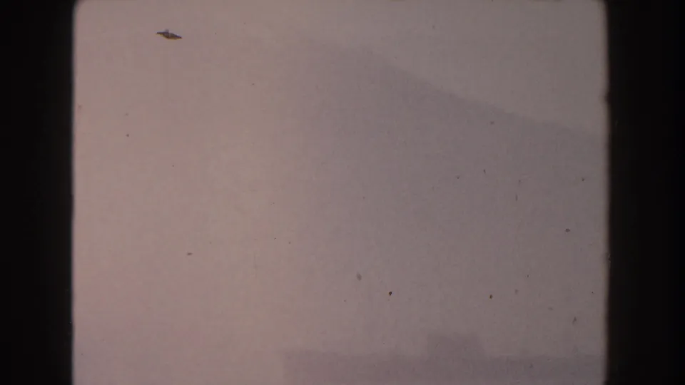 A small dark shape, possibly a distant ship, appears near the top of a hazy 1959 Pisa sky in soft 8mm color.