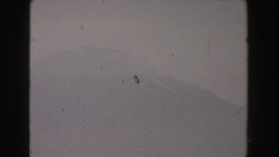 A faint mountain or hillside form rests below a pale cloudy sky in this soft 1959 Pisa 8mm home-movie frame.