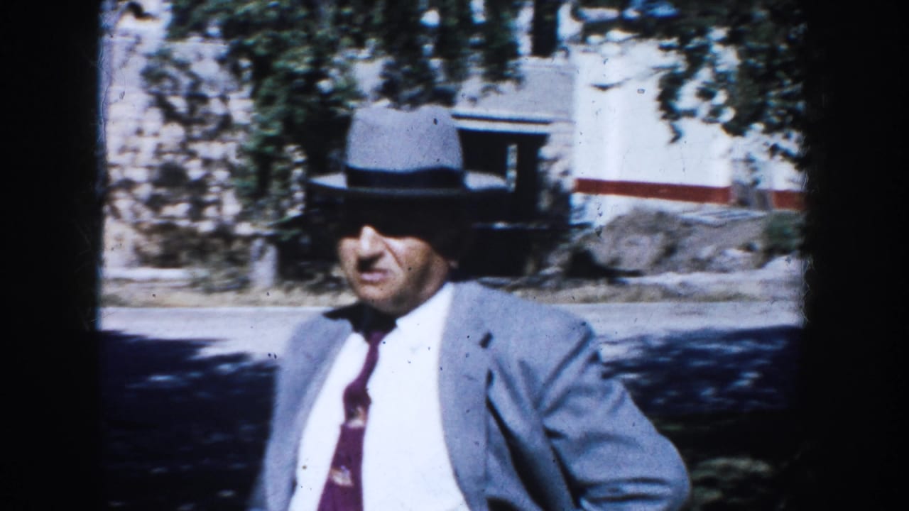 Adult man in a light gray suit, dark tie, and fedora walks through a sunlit South Dakota residential setting in 1953.